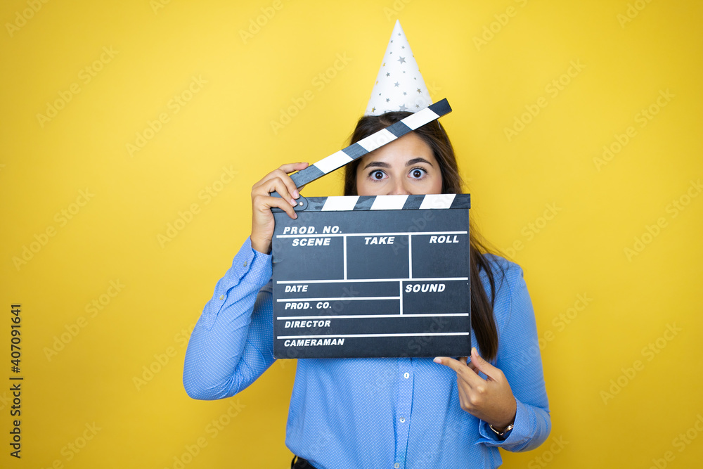Young caucasian woman wearing a birthday hat over isolated yellow background holding clapperboard very happy having fun Young caucasian woman wearing a birthday hat over isolated yellow background holding clapperboard very happy having fun