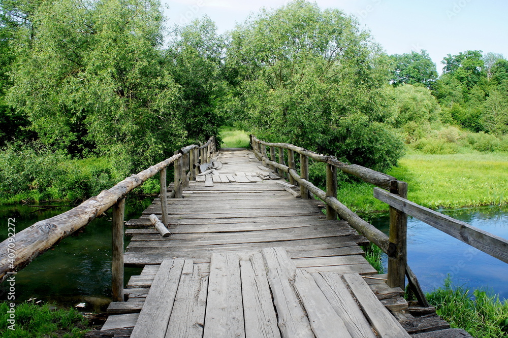 old wooden bridge across the river on a beautiful summer day and the clear water of the river and green trees