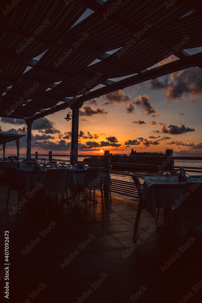 Sunset over water from the dining area of a sea front restaurant in southern Italy.Tables ready for service, silhouettes, amazing colored sky and sea.