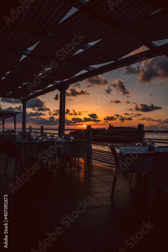 Sunset over water from the dining area of a sea front restaurant in southern Italy.Tables ready for service, silhouettes, amazing colored sky and sea.