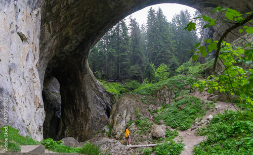 Lonely woman standing on wonderful bridge in Bulgaria. Famous and mysterious open wide cave. Magnificent rock formation and girl walking on a tour alone in vacation. stone arch with ecosystem