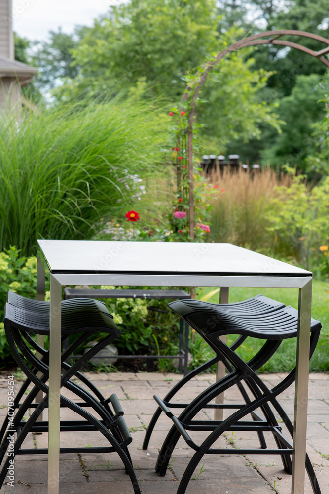 White contemporary table and bronze stools in the garden surrounded by ornamental grasses, miscanthus, reed grasses and zinnias