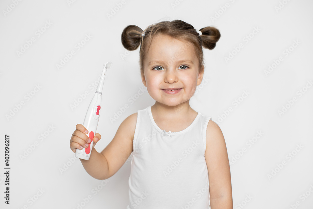 Promo of healthy teeth and oral care, prevention of caries concept. Studio portrait of smiling little happy 3 years old girl with an electric toothbrush on a white background Promo of healthy teeth and oral care, prevention of caries concept. Studio portrait of smiling little happy 3 years old girl with an electric toothbrush on a white background