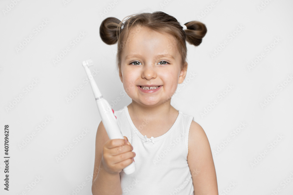 Health care, kid dental hygiene, closeup, copy space. A little girl with blonde hair showing her healthy teeth to camera, holding modern electric toothbrush in hands. Isolated on white background Health care, kid dental hygiene, closeup, copy space. A little girl with blonde hair showing her healthy teeth to camera, holding modern electric toothbrush in hands. Isolated on white background