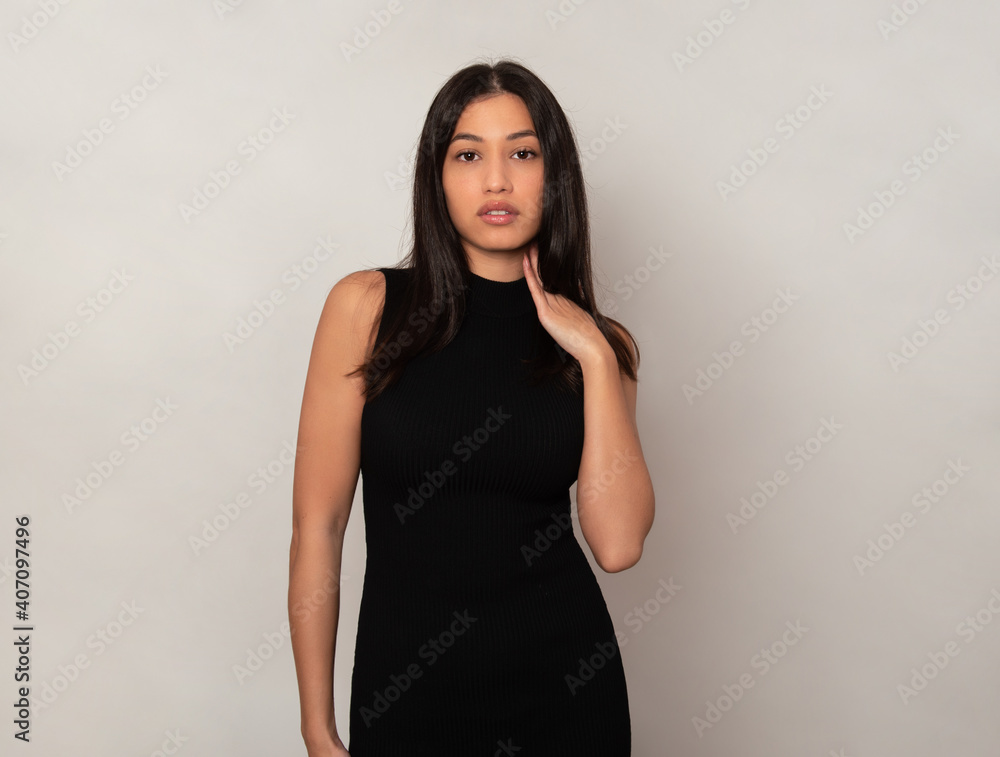 Beautiful young woman with long black hair posing in dress on grey background Beautiful young woman with long black hair posing in dress on grey background