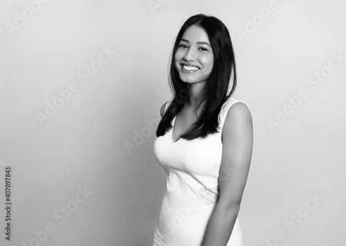 Beautiful young woman with long black hair posing in dress on grey background © Anetta