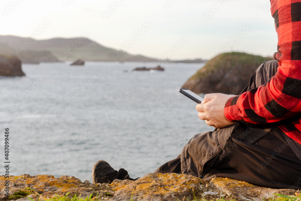 unrecognizable person sitting in front of the sea using his smartphone. communications concept.