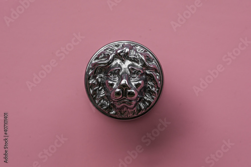 Solid metal silver coloured vintage style lion head handle against a pink painted door.