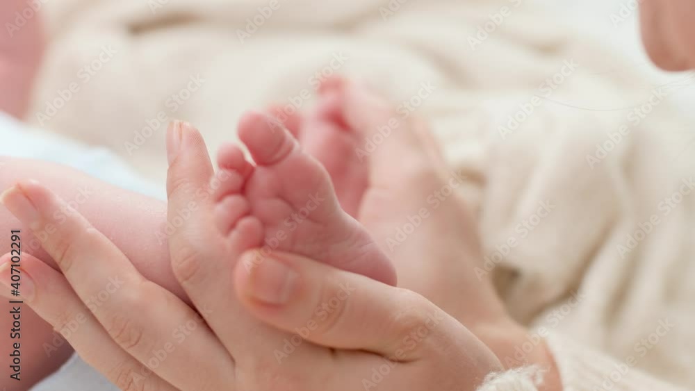 Closeup shot of young mother gently holding and touching little feet of her newborn baby boy lying in bed. Concept of family happiness and loving parents with little children Closeup shot of young mother gently holding and touching little feet of her newborn baby boy lying in bed. Concept of family happiness and loving parents with little children