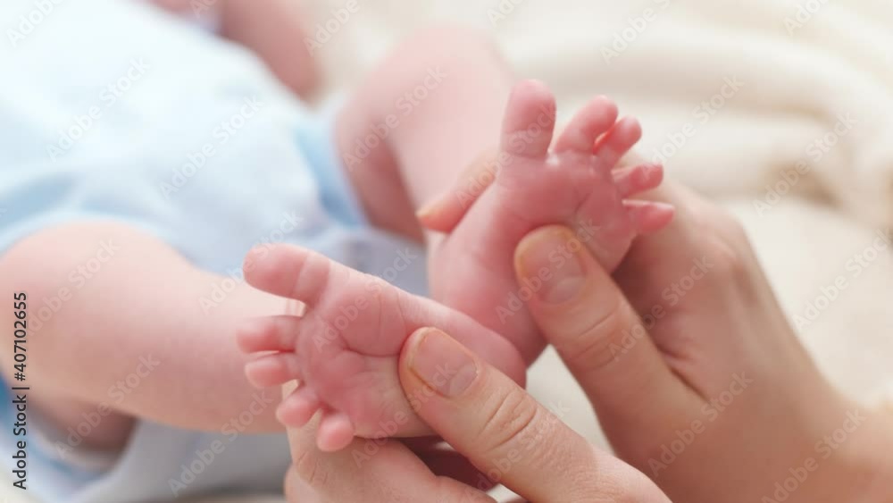 Closeup of young caring and loving mother massaging and stroking little feet of her newborn baby son lying in bed. Concept of family happiness and loving parents with little children. Baby massage and Closeup of young caring and loving mother massaging and stroking little feet of her newborn baby son lying in bed. Concept of family happiness and loving parents with little children. Baby massage and