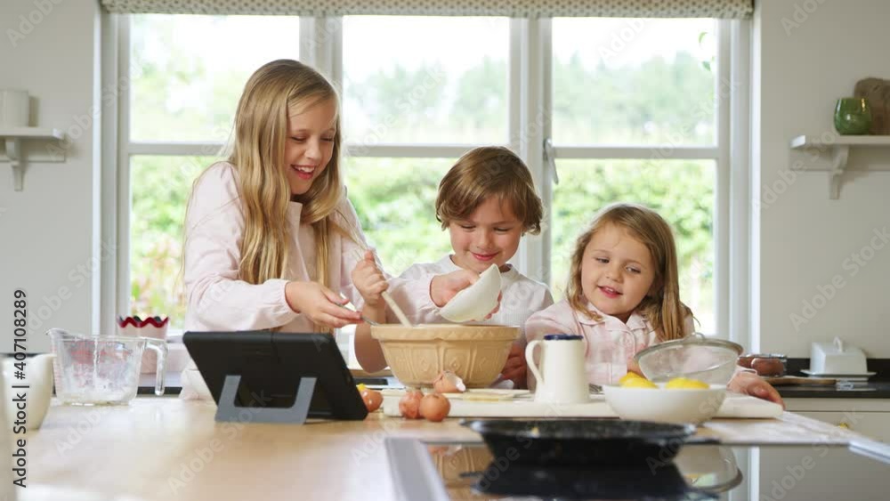Children in pyjamas baking in kitchen at home whilst following recipe on digital tablet - shot in slow motion Children in pyjamas baking in kitchen at home whilst following recipe on digital tablet - shot in slow motion