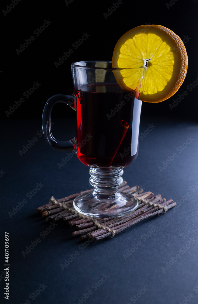 Hot mulled wine in a tall glass mug with orange straws on a dark background with copy space Hot mulled wine in a tall glass mug with orange straws on a dark background with copy space