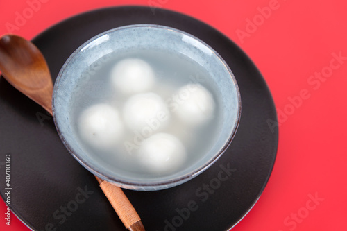 A bowl of Yuanxiao or Tangyuan and spoon in a black tray on a red background