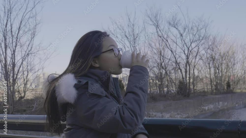 Asian woman takes a sip of hot chocolate while looking into the distance. Asian woman takes a sip of hot chocolate while looking into the distance.