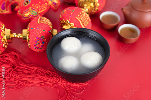 A bowl of Yuanxiao or Tangyuan and tea on a festive red background photo