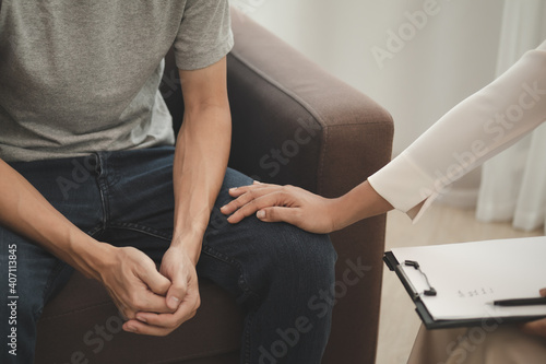 Young asian man suffers from a mental who needs to therapy with a psychologist while sitting on couch to consult  psychiatrist has encouragement the patient by touching to make his feel relaxed.