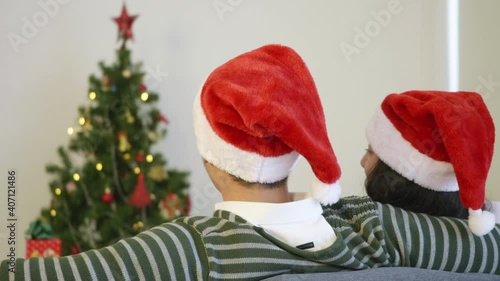 Wallpaper Mural Happy Asian beautiful young family couple husband and wife sitting on sofa wearing a santa hat in front of fireplace at warm home Christmas winter hugging living room, back view,  slow motion Torontodigital.ca