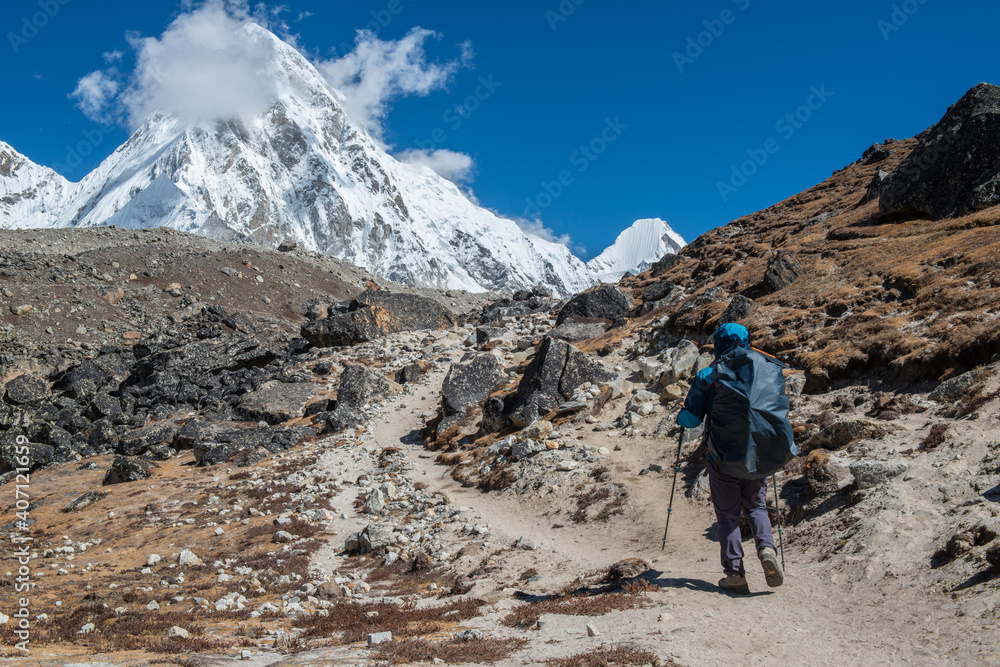 Trekker walking on rugged landscape with the view of Mt.Pumori (7,161 metres) one of the very famous seven-thousanders in the world during trekking to Everest base camp in Nepal.