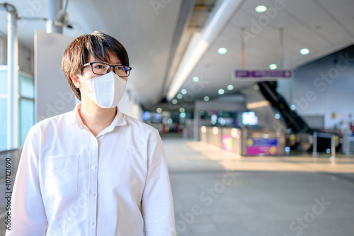 Asian man wearing face mask at skytrain station or urban train platform. Coronavirus (COVID-19) outbreak prevention in public transportation. Health awareness for PM2.5 air pollution protection.