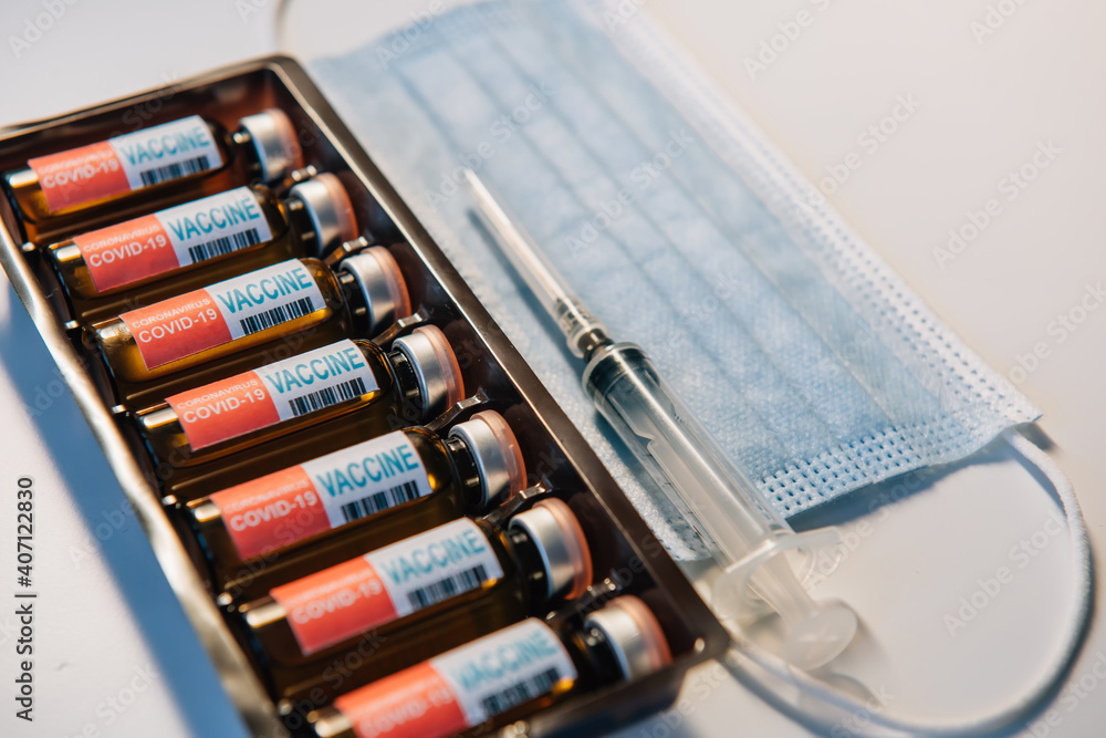 Coronavirus vaccine in box, close-up. Vials of medicine for covid19, syringe, medical face mask. Label with inscription. Concept of mass immunization from viral disease. Coronavirus vaccine in box, close-up. Vials of medicine for covid19, syringe, medical face mask. Label with inscription. Concept of mass immunization from viral disease.
