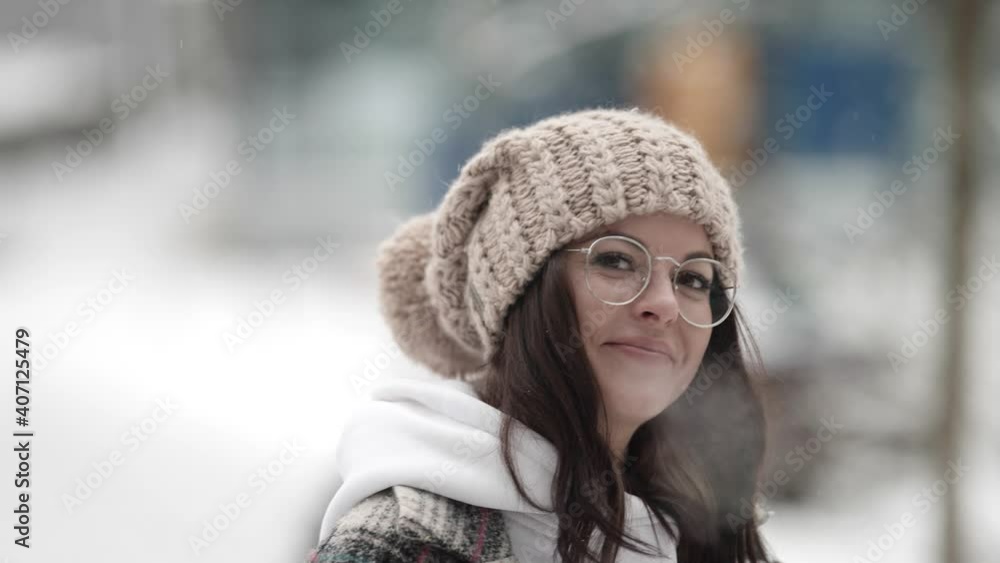 Portrait of a happy young dark-haired woman in round glasses and a plaid coat walking on a frosty street on a snowy winter day. Portrait of a happy young dark-haired woman in round glasses and a plaid coat walking on a frosty street on a snowy winter day.