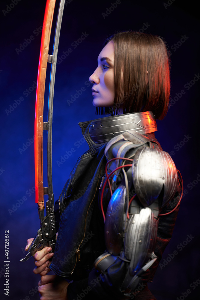 Fototapeta premium Seductive female assassin poses in dark background looking at her glowing sword. Profile of a military woman from the future in cyberpunk style.