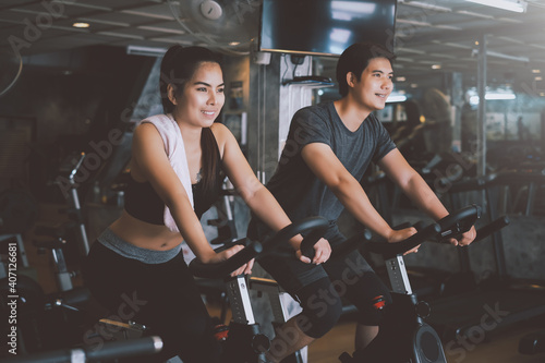 Fototapeta Naklejka Na Ścianę i Meble -  Asian man and woman they are enjoys cycling in the gym because it keeps his legs strong and healthy.