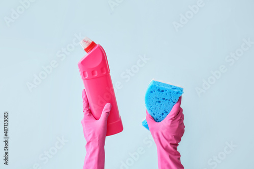 Hands in rubber gloves with cleaning sponge and detergent on color background