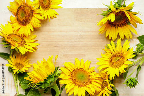 Frame made of beautiful sunflowers on light wooden background