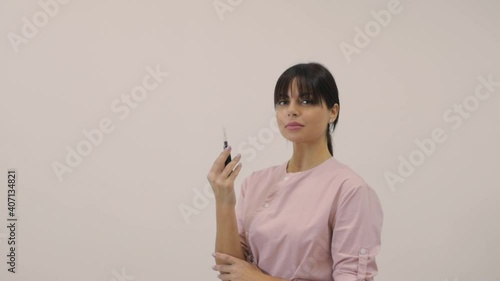 Happy female master in pink uniform shows tattoo machine posing for camera on beige background with space for design slow motion