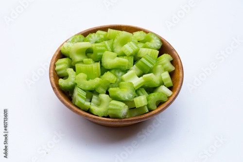 Slices of celery in wooden bowl on white background.