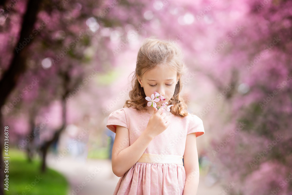 Cute little pensive girl with handmade hair wreath on her head smelling flowers in the spring blossom garden, close-up Cute little pensive girl with handmade hair wreath on her head smelling flowers in the spring blossom garden, close-up