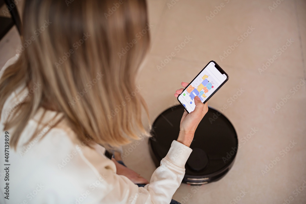 Robotic vacuum cleaner cleaning the room while woman relaxing. Woman controlling vacuum with remote control. Smart home concept Robotic vacuum cleaner cleaning the room while woman relaxing. Woman controlling vacuum with remote control. Smart home concept