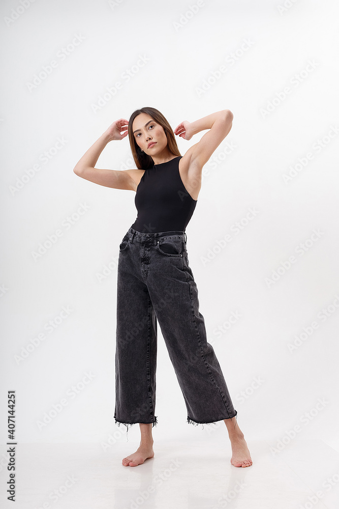 portrait of young attractive asian woman with long hair in black bodysuit, jeans, isolated on white studio background. skinny pretty female posing on cyclorama. model tests of beautiful lady portrait of young attractive asian woman with long hair in black bodysuit, jeans, isolated on white studio background. skinny pretty female posing on cyclorama. model tests of beautiful lady