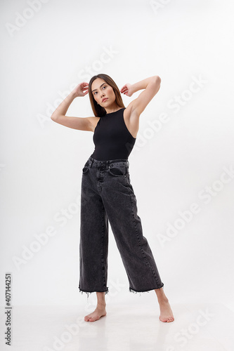 portrait of young attractive asian woman with long hair in black bodysuit, jeans, isolated on white studio background. skinny pretty female posing on cyclorama. model tests of beautiful lady © Artem Zatsepilin