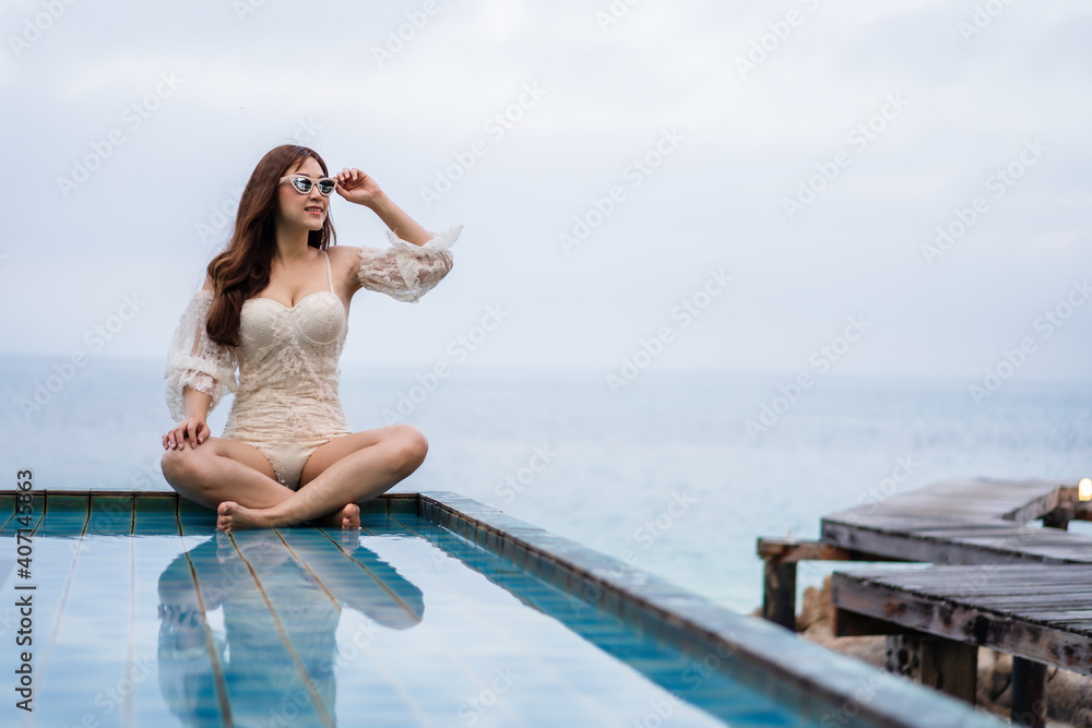 woman sitting on edge of swimming pool and looking to the sea
