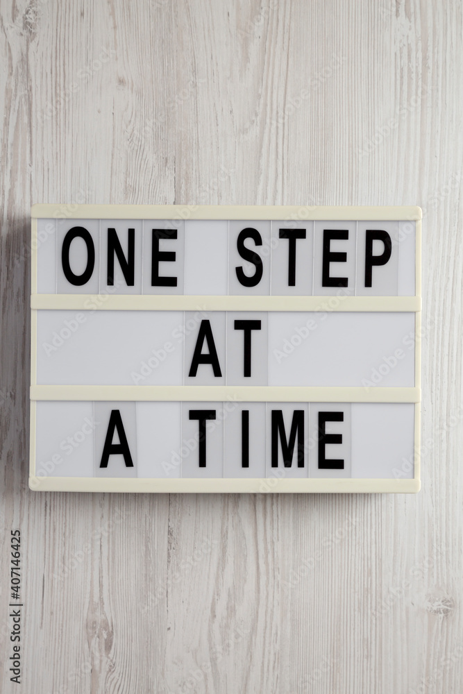 'One step at a time' on a lightbox on a white wooden surface, top view. Flat lay, overhead, from above. 'One step at a time' on a lightbox on a white wooden surface, top view. Flat lay, overhead, from above.