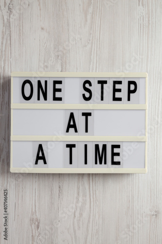 'One step at a time' on a lightbox on a white wooden surface, top view. Flat lay, overhead, from above.