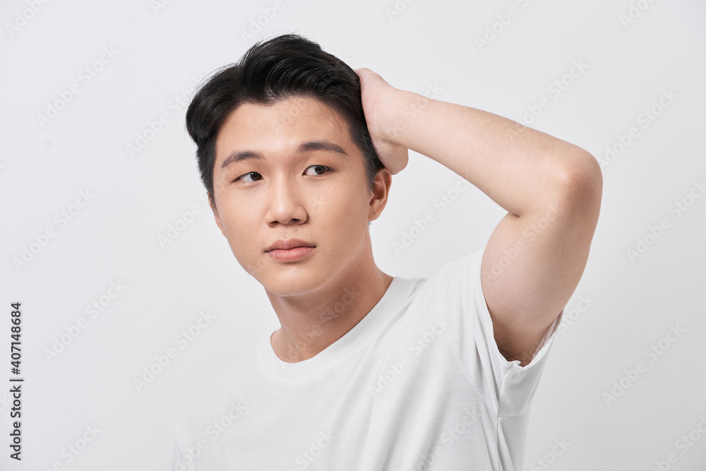 Confident smiling handsome young man in white t shirt. standing on the pure background, fixing his perfect hairstyle Confident smiling handsome young man in white t shirt. standing on the pure background, fixing his perfect hairstyle