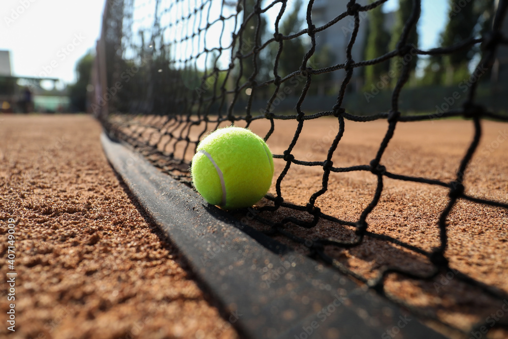 Tennis ball near net on clay court, closeup