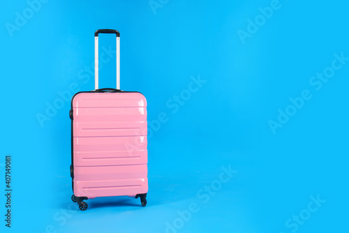 Travel pink suitcase on light blue background, space for text. Summer vacation