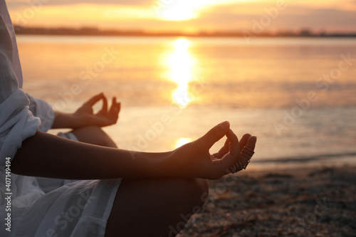 Young woman meditating near river at sunset, closeup. Nature healing power