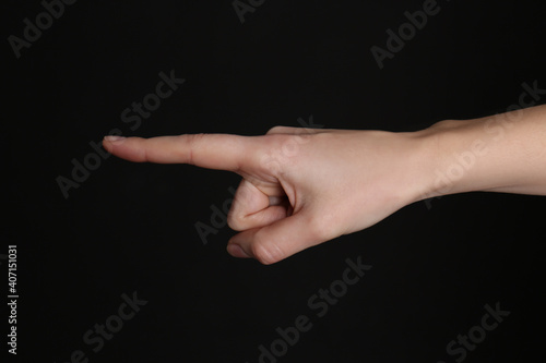 Woman pointing at something on black background, closeup. Finger gesture