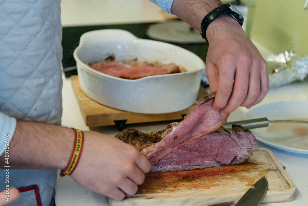 Midsection of man cutting roast meat on table at kitchen