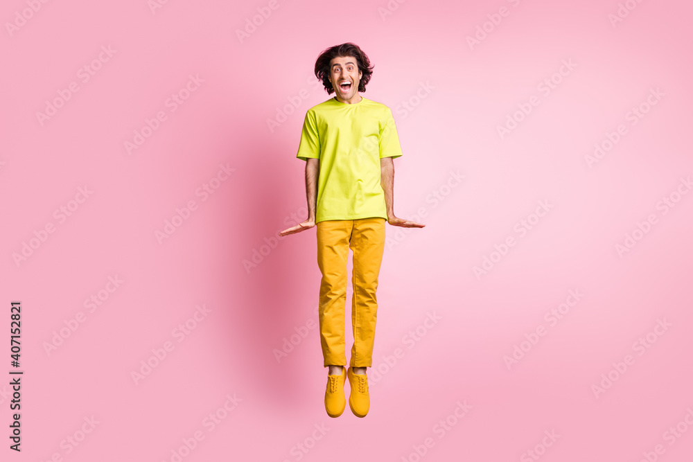 Full size photo of optimistic curly hairdo guy jumping yell wear t-shirt trousers sneakers isolated on pastel pink background Full size photo of optimistic curly hairdo guy jumping yell wear t-shirt trousers sneakers isolated on pastel pink background