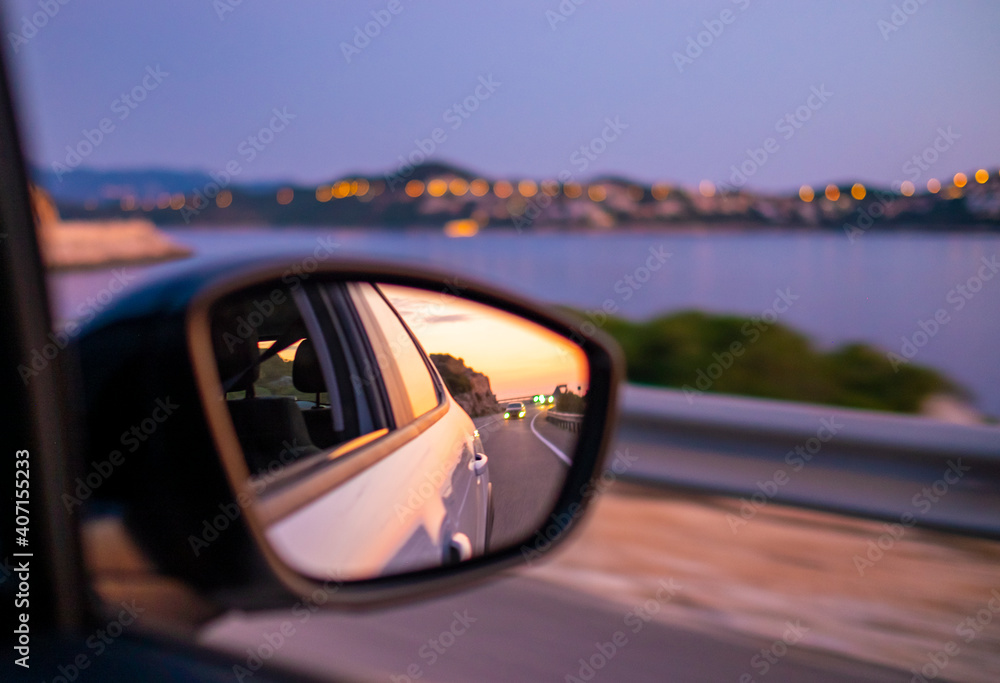 Traveling by car along beautiful coast at night. Reflection of sunset at side mirror.