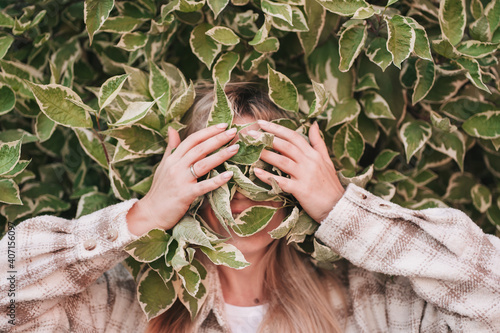 Portrait of a girl covering her face with green leaves.