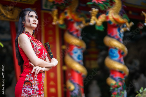 Portrait beautiful smiles Asian young woman wearing red traditional Chinese cheongsam decoration and holding a Chinese Fanning for Chinese New Year Festival at Chinese shrine in Thailand