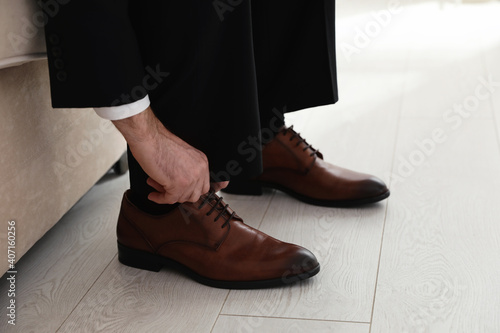 Groom putting on elegant wedding shoes indoors, closeup
