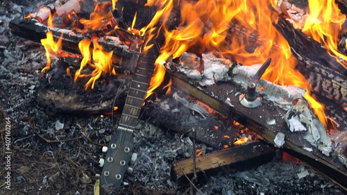 An acoustic guitar is burned in a large fire. Burning trash.